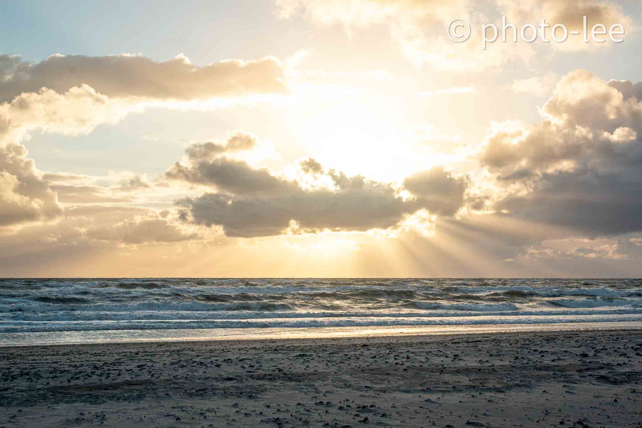 Hinter einer Wolke tun sich die Sonnenstrahlen auf und verbreiten sich über dem Meer
